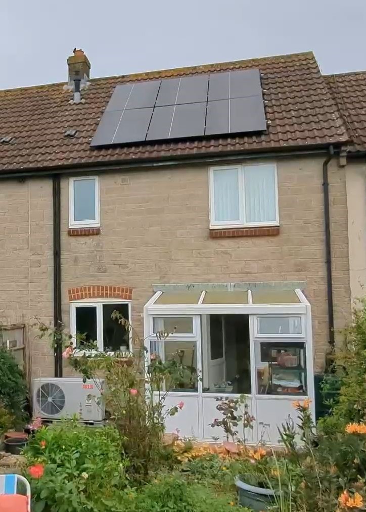 House with roof-mounted solar panels and an air source heat pump unit at ground level
